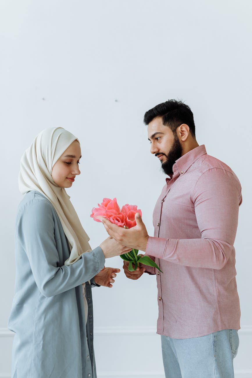 man in pink button up shirt giving flowers to a woman wearing white hijab